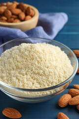 Fresh almond flour in bowl and nuts on blue wooden table, closeup