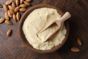 Fresh almond flour, scoop in bowl and nuts on wooden table, flat lay