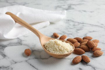 Spoon with fresh almond flour and nuts on white marble table, closeup