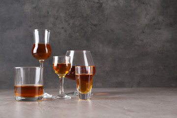 Many different liqueurs in glasses on grey textured table. Space for text