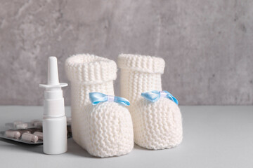 Baby`s booties, nasal spray and pills on grey table, closeup