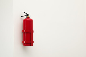 Fire extinguisher on light wall, space for text