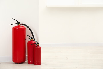 Fire extinguishers on floor near light wall indoors, space for text