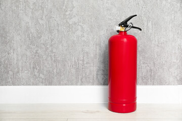 Fire extinguisher on floor near grey wall, space for text