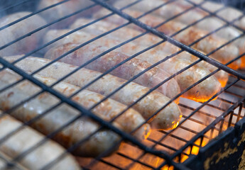 Close-up of sausages grilling on a hot grill with smoke rising from the flames.