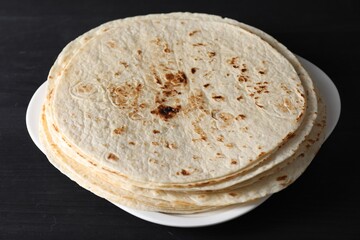 Many tasty homemade tortillas on black wooden table, closeup