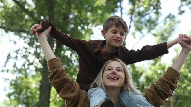 Stylish and happy european mother with son on shoulders at outdoor in summer time