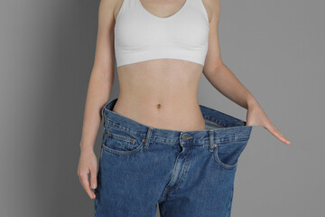 Woman in big jeans showing her slim body on grey background, closeup