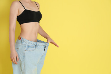 Woman in big jeans showing her slim body on yellow background, closeup. Space for text