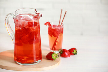 Tasty strawberry lemonade in jug, glass and berries on white wooden table, space for text