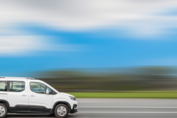 White compact van drives down the street, speed blurred background with free space for text, copy...