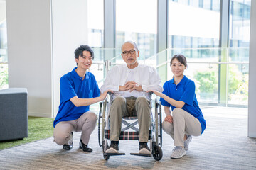 介護施設の車いすに乗ったシニア男性と男女スタッフ