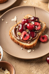 Breakfast toast with chocolate paste, sweet cherry and almond petals on beige textured background close up. Breakfast for kids