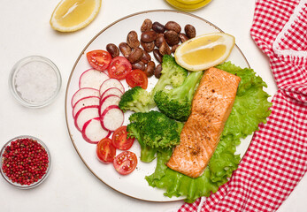 Healthy lunch with grilled salmon on green lettuce, next to vegetables, tomatoes, radishes, broccoli and a portion of beans.