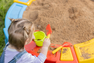 A young girl is playing in the sand box with a shovel and a cup.