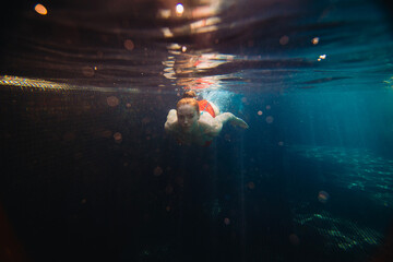 Beautiful red-haired woman swims underwater in the pool.