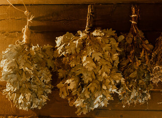 A close-up shot of three bundles of oak and birch branches, commonly used for bathing in a traditional Russian banya, hanging from the wooden walls.