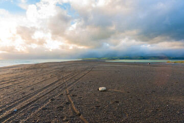 Pumice stone and vehicle tracks along wide stony beach on overcast day.