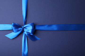 Bright satin ribbon with bow on blue background, top view