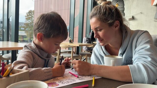 Young mother and her son sitting in cafe and coloring together