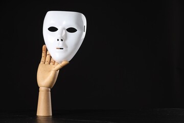 Wooden mannequin hand holding plastic mask on black background, space for text. Theatrical...