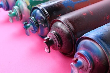 Many spray paint cans on pink background, closeup