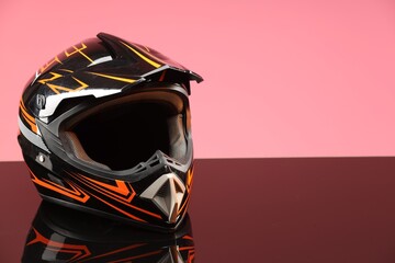 Modern motorcycle helmet with visor on mirror surface against pink background. Space for text