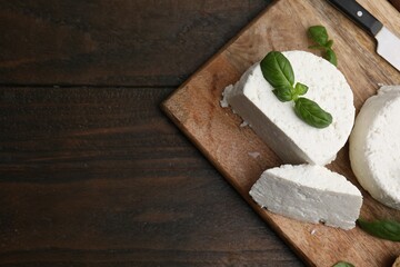 Fresh ricotta (cream cheese), basil, bread and knife on wooden table, top view. Space for text