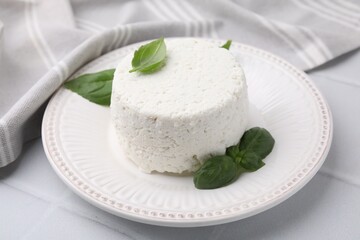 Fresh ricotta (cream cheese) and basil on light table, closeup