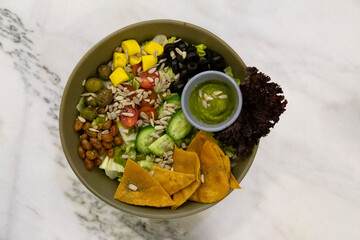 A bowl of fresh salad with several vegetables, fruits and pesto sauce