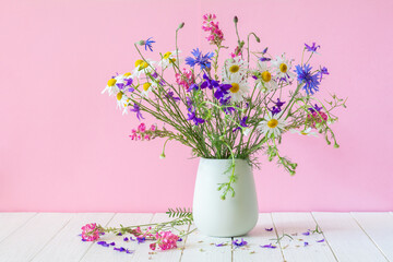 Bouquet of white daisies and other wildflowers in a white vase on a pink background