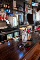 Glass of cocktail on bar counter with moody dark background. Bartender's place in a pub with shelves and bottles of alcohol