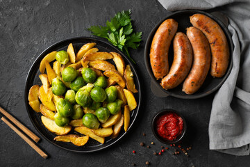 Bavarian sausage and brussels sprouts, parsley, potatoes on black plate or pan, tomato sauce