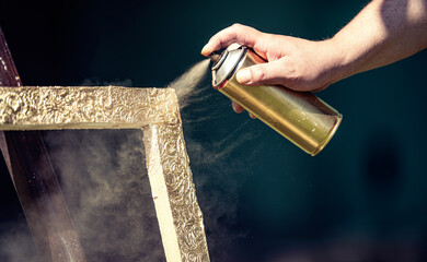 Spraying golden paint on frame. preparing for framing pictures.