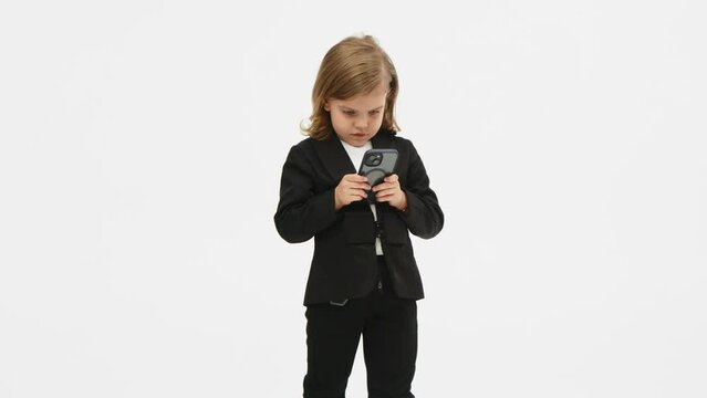 Little business girl on a white background in the studio clicks on a mobile phone and shows a "super" gesture of approval. Concept of business, deal and modern technology.
