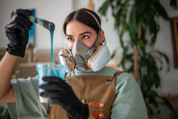 Professional female artist stirs epoxy resin, evaluates thickness and necessary consistency to work...