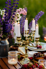 Romantic surprise, marriage proposal. Elegant decoration. Private wedding party for two, table set with floral decor, chandelier, fruits, wine in field or meadow. Summer, sunset, golden hour