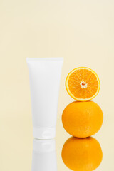 Vertical mockup of white face cream tube and oranges reflected in mirror on beige isolated background. Concept of moisturizing and skin care, beauty products.