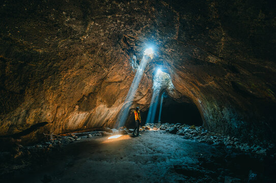 Sunbeams shooting down from a skylight inside Skylight Cave in Oregon. Enjoyment - a woman enjoying sunlight pouring into a cave. 
