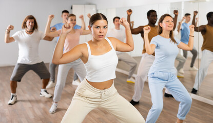 Happy flexible multiethnic men and women exercising active moves with group of people in dance...