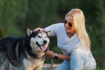 Young blonde girl with a Siberian Husky dog ​​on nature in summer, close-up photo.