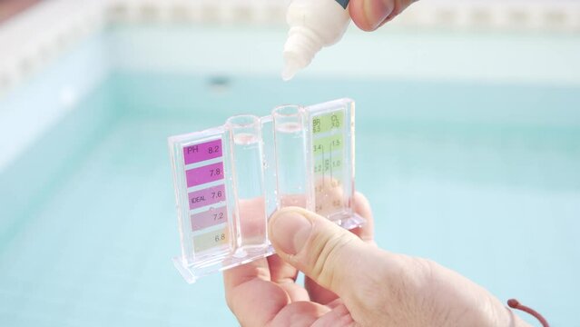 The hand of the maintenance person with a test-tube, pouring drops to check the pH and chlorine of the water in a swimming pool, in the background the blue of the pool.