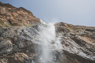 Waterfall against the sky in the mountains, water falls from the top of the cliff