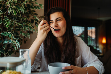 One young caucasian woman is eating corn flex breakfast at home before work	