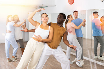 Joyful young adult couples learning passionate pair dancing during practicing in choreography class