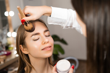 Make up artist applying powder with a brush to a blonde woman at beauty salon