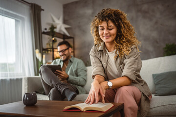 Obraz premium Girlfriend read a book while his boyfriend use tablet at home