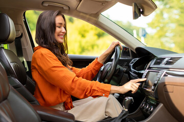 Happy European woman driving car and choosing road playlist for listening to music on auto audio...