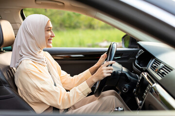Muslim woman driving her luxury car, traveling, using automobile for transportation to get to destination, holding the steering wheel