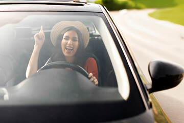 Overjoyed lady enjoying driving car and listening her playlist, try dancing and holding steering...